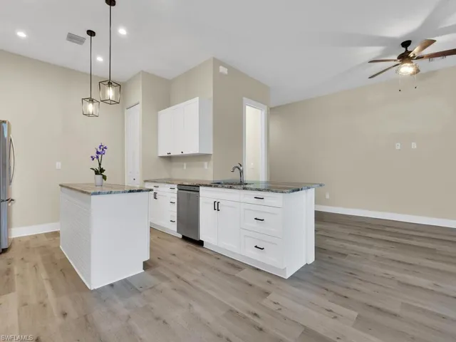 Kitchen with dark stone countertops, appliances with stainless steel finishes, white cabinetry, and light wood-type flooring