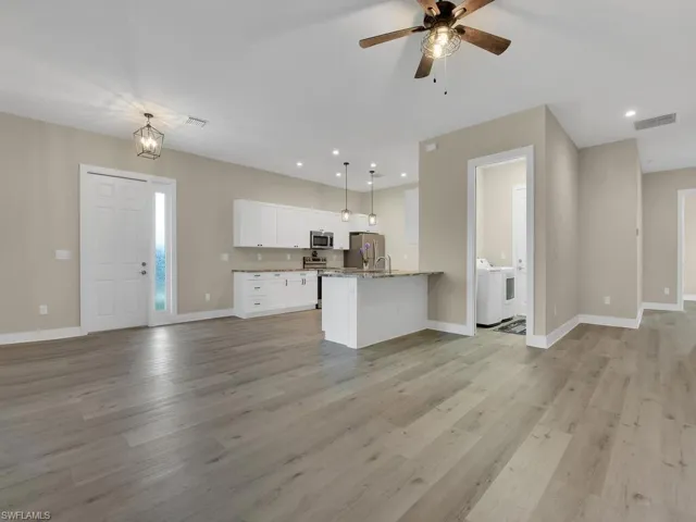 Kitchen with hanging light fixtures, light hardwood / wood-style flooring, white cabinets, and independent washer and dryer