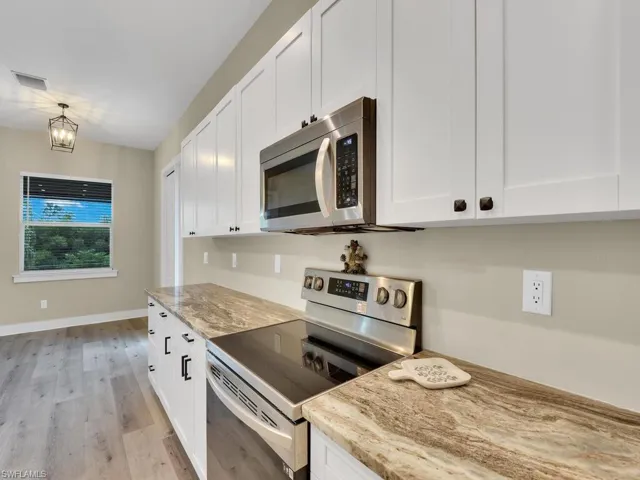 Kitchen with light hardwood / wood-style floors, an inviting chandelier, light stone counters, white cabinets, and appliances with stainless steel finishes