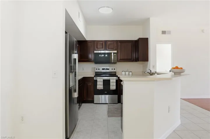 Kitchen with stainless steel appliances, light countertops, light tile patterned floors, dark brown cabinetry, and a peninsula