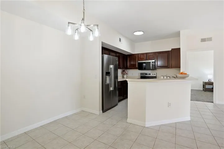 Kitchen featuring appliances with stainless steel finishes, pendant lighting, dark brown cabinets, light countertops, and light tile patterned floors