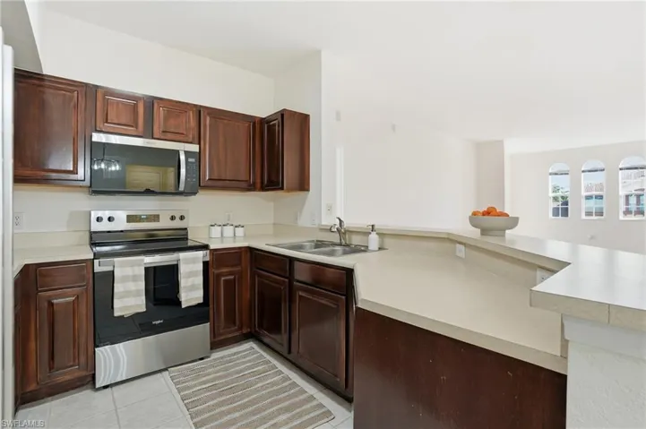 Kitchen with appliances with stainless steel finishes, light countertops, light tile patterned flooring, a peninsula, and dark brown cabinets