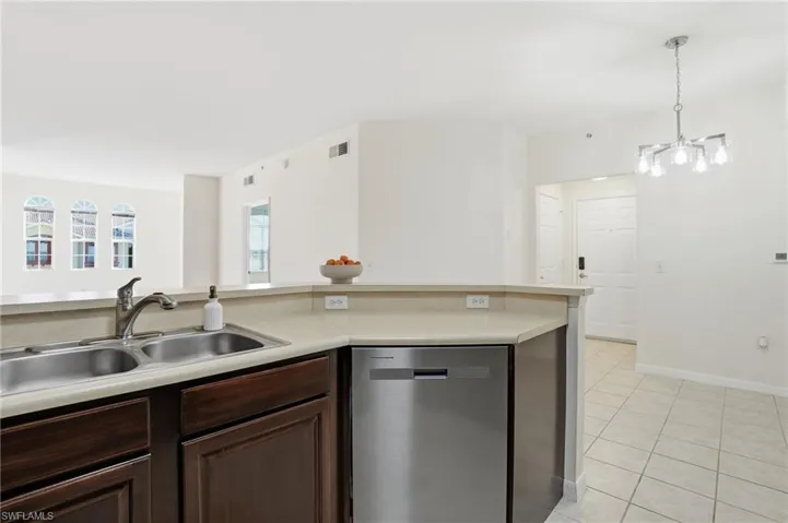 Kitchen with dishwasher, light countertops, light tile patterned floors, decorative light fixtures, and dark brown cabinets