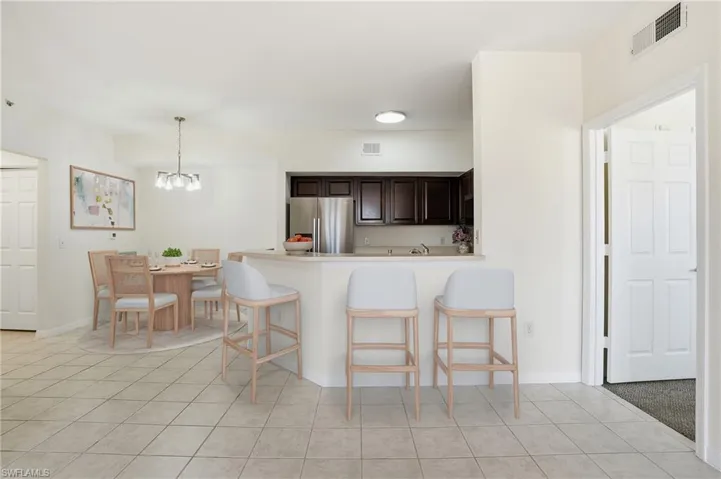 Kitchen with dark brown cabinets, light tile patterned floors, a kitchen bar, and stainless steel fridge with ice dispenser