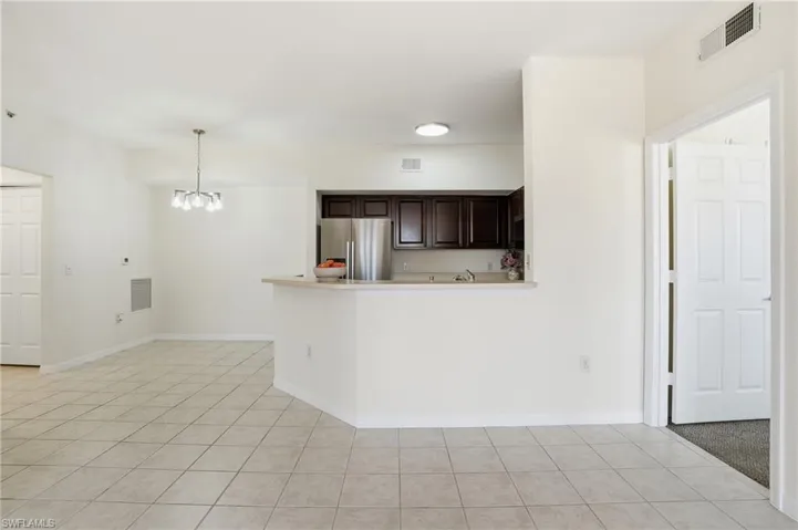 Kitchen featuring dark brown cabinets, freestanding refrigerator, light tile patterned floors, a chandelier, and decorative light fixtures