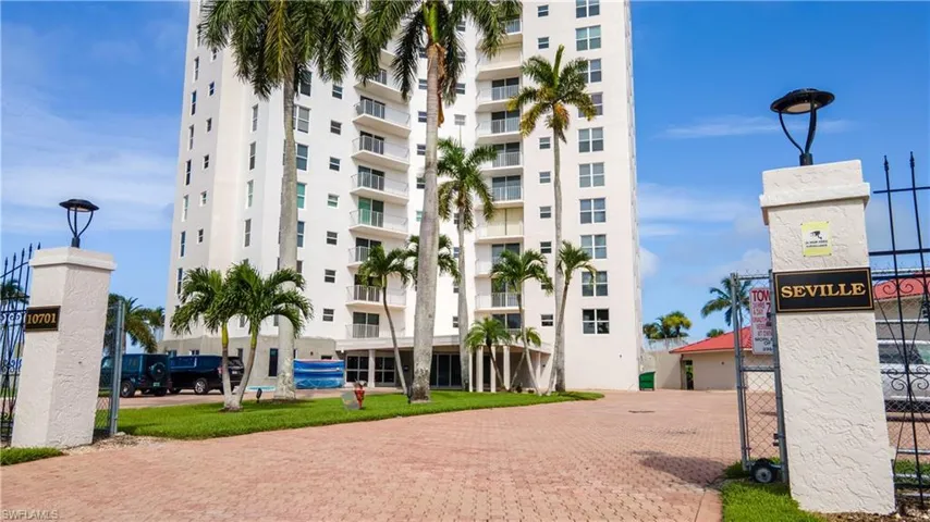High-rise residential building featuring multiple balconies, a paver driveway, and mature palm trees