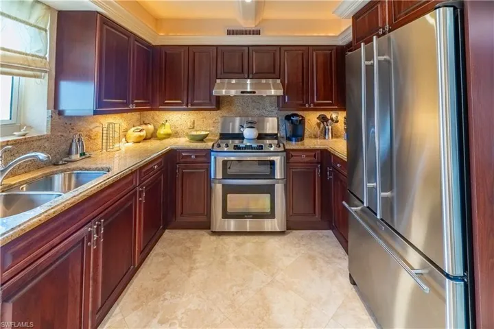 U-shaped kitchen featuring wood cabinetry, light-toned countertops, stainless steel appliances, and a double basin sink