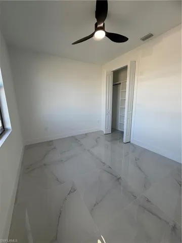 Unfurnished bedroom featuring light marble finish flooring, ceiling fan, and a closet