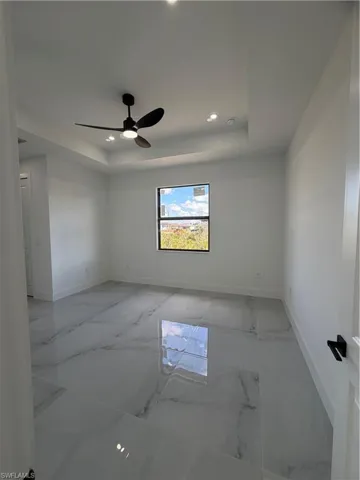 Unfurnished room featuring marble tiled flooring, a raised ceiling, recessed lighting, and ceiling fan