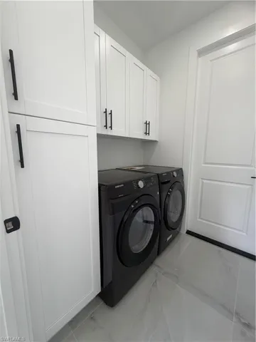 Washroom with light marble finish floors, cabinet space, and washer and dryer
