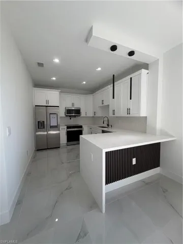 Kitchen with white cabinetry, refrigerator, a peninsula, light stone counters, and recessed lighting