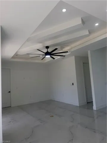 Unfurnished room with a tray ceiling, recessed lighting, light marble finish floors, and a ceiling fan