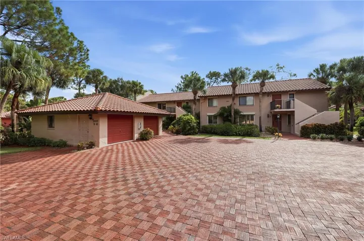 Red clay tile roof, stucco exterior, red brick paver driveway, lush landscaping, and a two-car garage