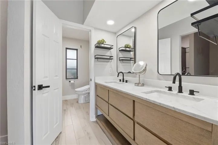 Dual vanity with stone countertop, integrated sinks, wood-finish cabinetry, and matte black fixtures