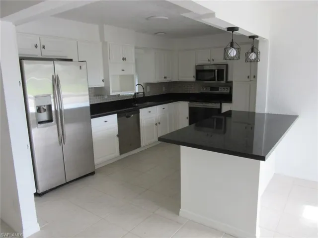 Kitchen featuring appliances with stainless steel finishes, decorative backsplash, white cabinets, and a peninsula