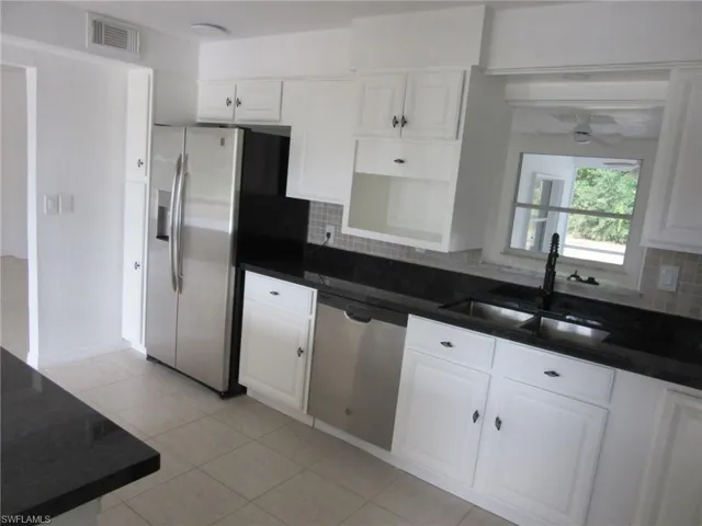 Kitchen with white cabinets, stainless steel appliances, backsplash, and light tile patterned floors