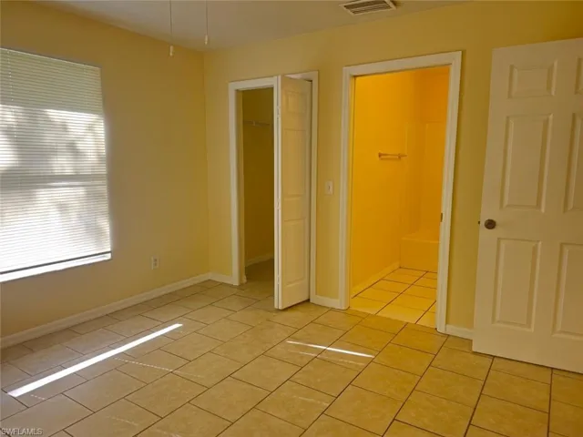 Unfurnished bedroom featuring light tile patterned flooring, a spacious closet, and connected bathroom
