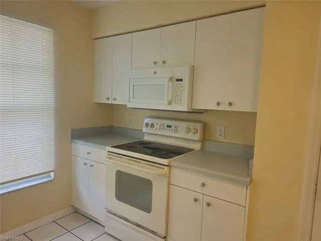 Kitchen featuring white appliances, light countertops, light tile patterned floors, and white cabinets