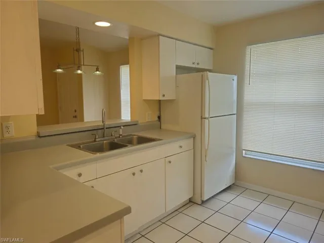 Kitchen featuring light countertops, light tile patterned flooring, white cabinets, freestanding refrigerator, and hanging light fixtures