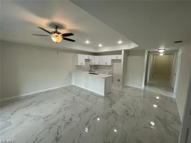 Kitchen with a peninsula, a tray ceiling, white cabinets, a ceiling fan, and light countertops