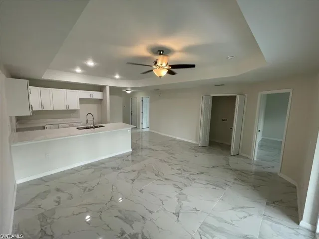 Kitchen featuring a raised ceiling, white cabinets, a peninsula, recessed lighting, and a ceiling fan
