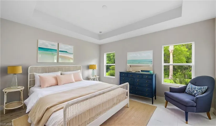 Spacious bedroom featuring a tray ceiling, light gray walls, two double-hung windows, and light wood-finish flooring