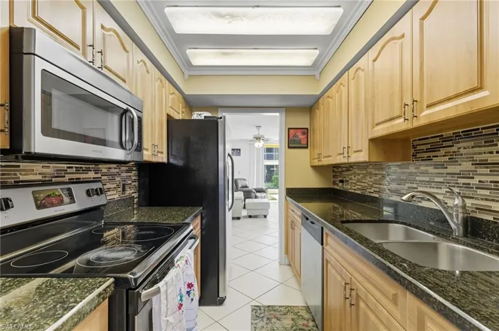 Kitchen with stainless steel appliances, tasteful backsplash, ornamental molding, light tile patterned flooring, and a ceiling fan