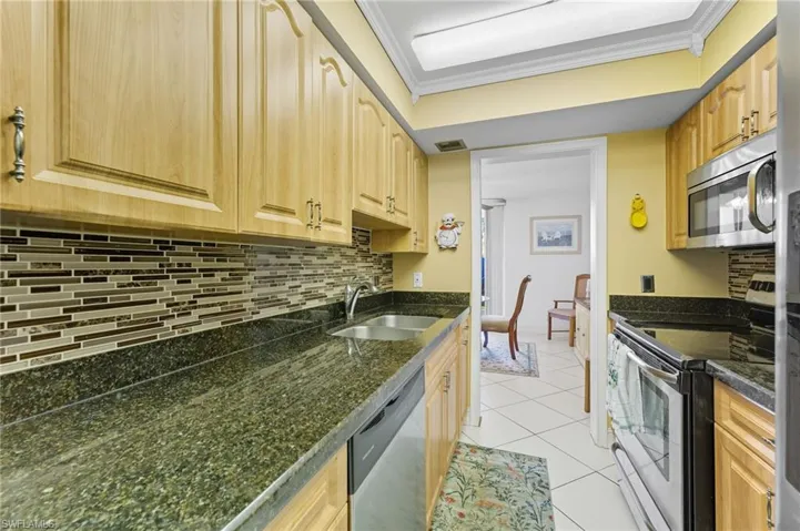 Kitchen featuring appliances with stainless steel finishes, decorative backsplash, light tile patterned flooring, crown molding, and dark stone counters