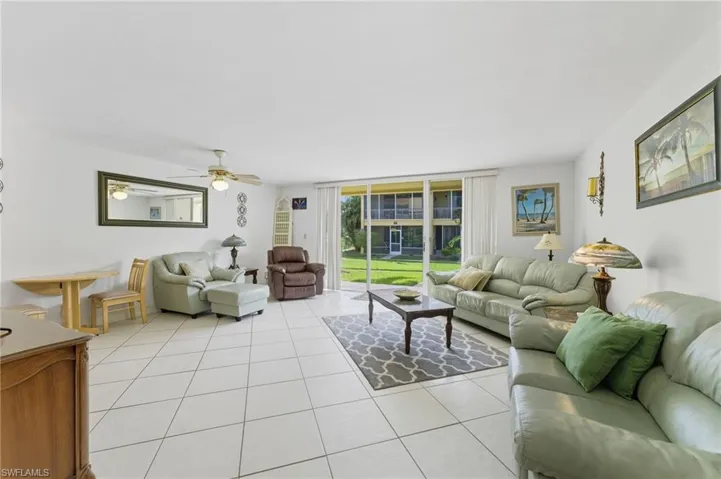 Living room with a wall of windows, light tile patterned floors, and ceiling fan
