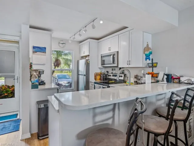 Kitchen featuring appliances with stainless steel finishes, light wood-type flooring, light countertops, a peninsula, and a kitchen bar