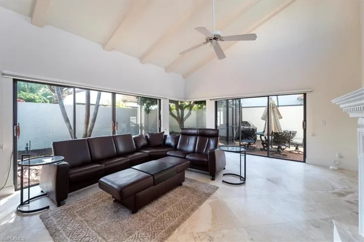 Living room with a premium fireplace, high vaulted ceiling, ceiling fan, and beam ceiling