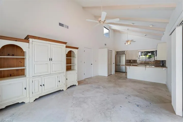 Unfurnished living room with beamed ceiling, ceiling fan, and high vaulted ceiling