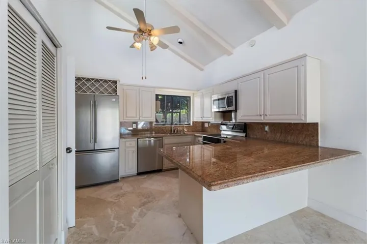 Kitchen featuring tasteful backsplash, appliances with stainless steel finishes, kitchen peninsula, beamed ceiling, and white cabinets