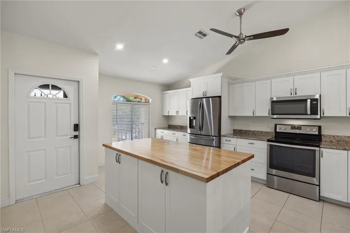 Open concept kitchen with large butcher block island, white cabinetry, stainless steel appliances, and vaulted ceiling