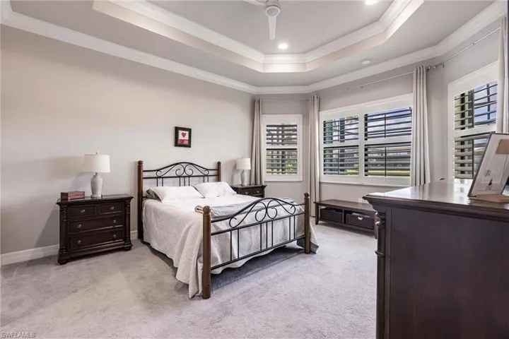 Bedroom featuring a tray ceiling, light colored carpet, ornamental molding, recessed lighting, and baseboards
