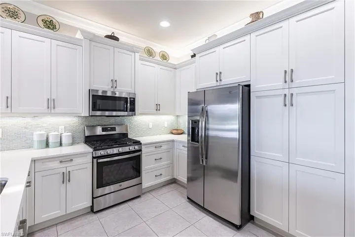 Kitchen with stainless steel appliances, light tile patterned floors, light countertops, tasteful backsplash, and white cabinetry