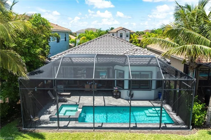Back of property with a tiled roof, a patio, a lanai, and a pool with connected hot tub