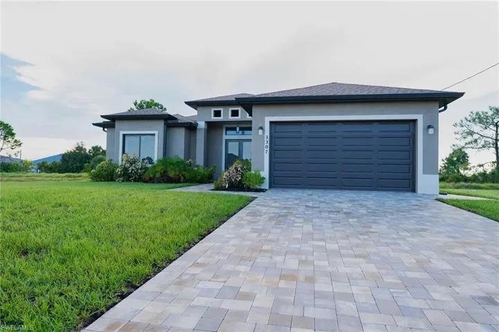 Prairie-style house with a front yard, decorative driveway, stucco siding, and an attached garage