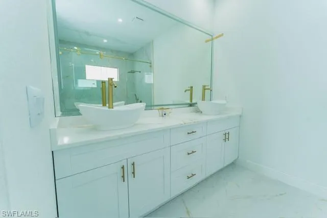 Bathroom featuring light marble finish floors, double vanity, and a marble finish shower