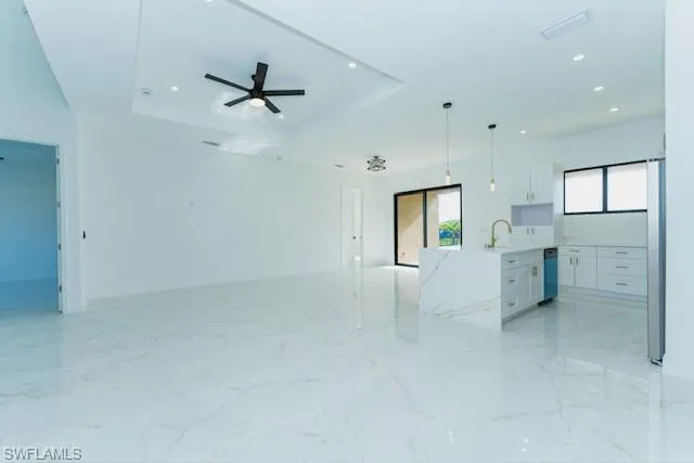 Unfurnished living room with light marble finish floors, recessed lighting, a tray ceiling, and a ceiling fan