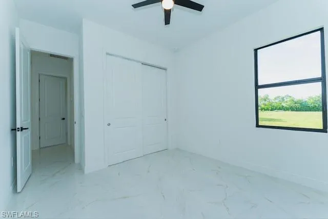 Unfurnished bedroom featuring light marble finish flooring, a closet, and ceiling fan