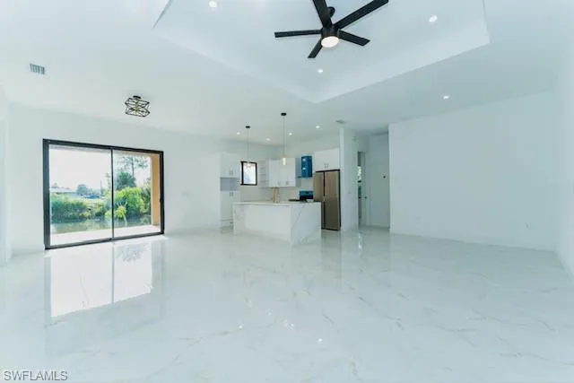 Unfurnished living room with a raised ceiling, light marble finish floors, recessed lighting, and ceiling fan