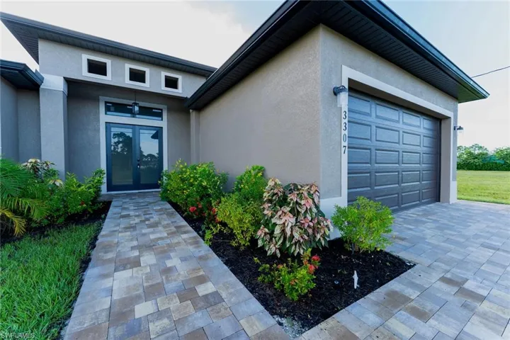 Property entrance with stucco siding, an attached garage, decorative driveway, and french doors