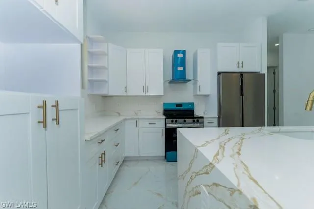 Kitchen featuring light stone countertops, open shelves, stainless steel appliances, white cabinets, and wall chimney exhaust hood