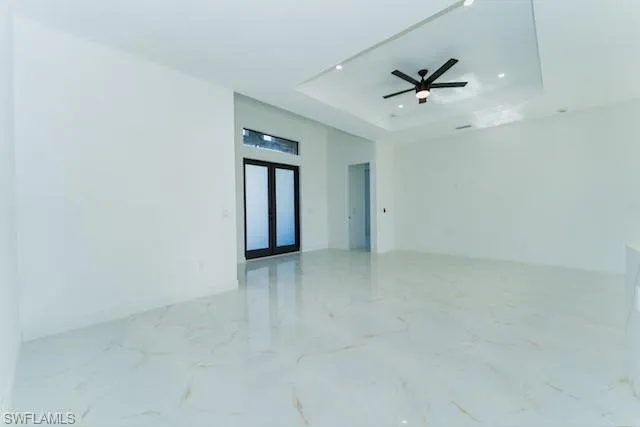 Empty room featuring a raised ceiling, light marble finish flooring, french doors, and a ceiling fan