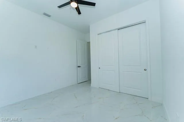 Unfurnished bedroom with light marble finish floors, a ceiling fan, and a closet