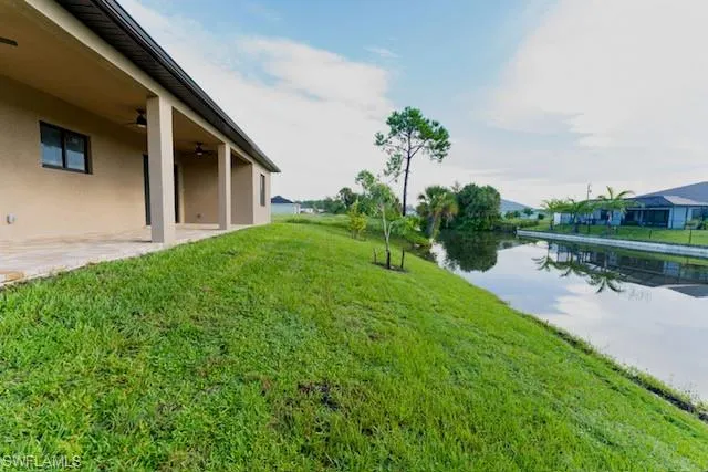 View of green lawn featuring ceiling fan, a patio, and a water view