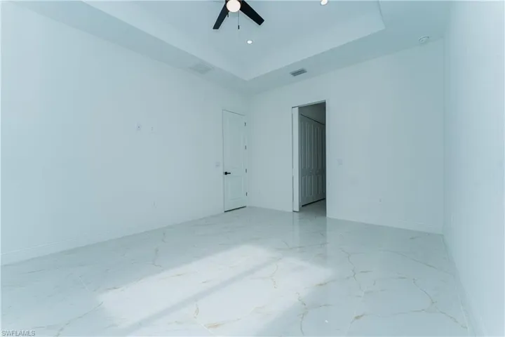 Spare room featuring a raised ceiling, light marble finish floors, ceiling fan, and recessed lighting