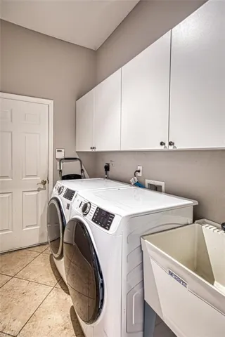 Washroom featuring independent washer and dryer, cabinet space, and light tile patterned floors