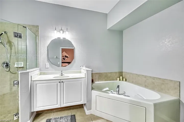 Full bath featuring vanity, a shower stall, a bath, light tile patterned floors, and a textured wall